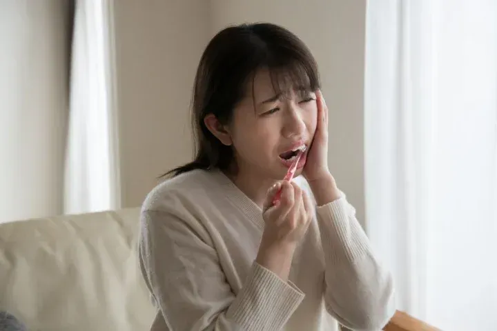 歯磨きをしながら歯を痛める女性