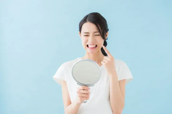 手鏡を持って歯の痛みを感じる女性