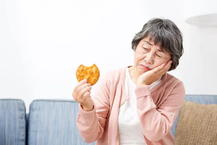 お煎餅を片手に歯を気にするおばあさん